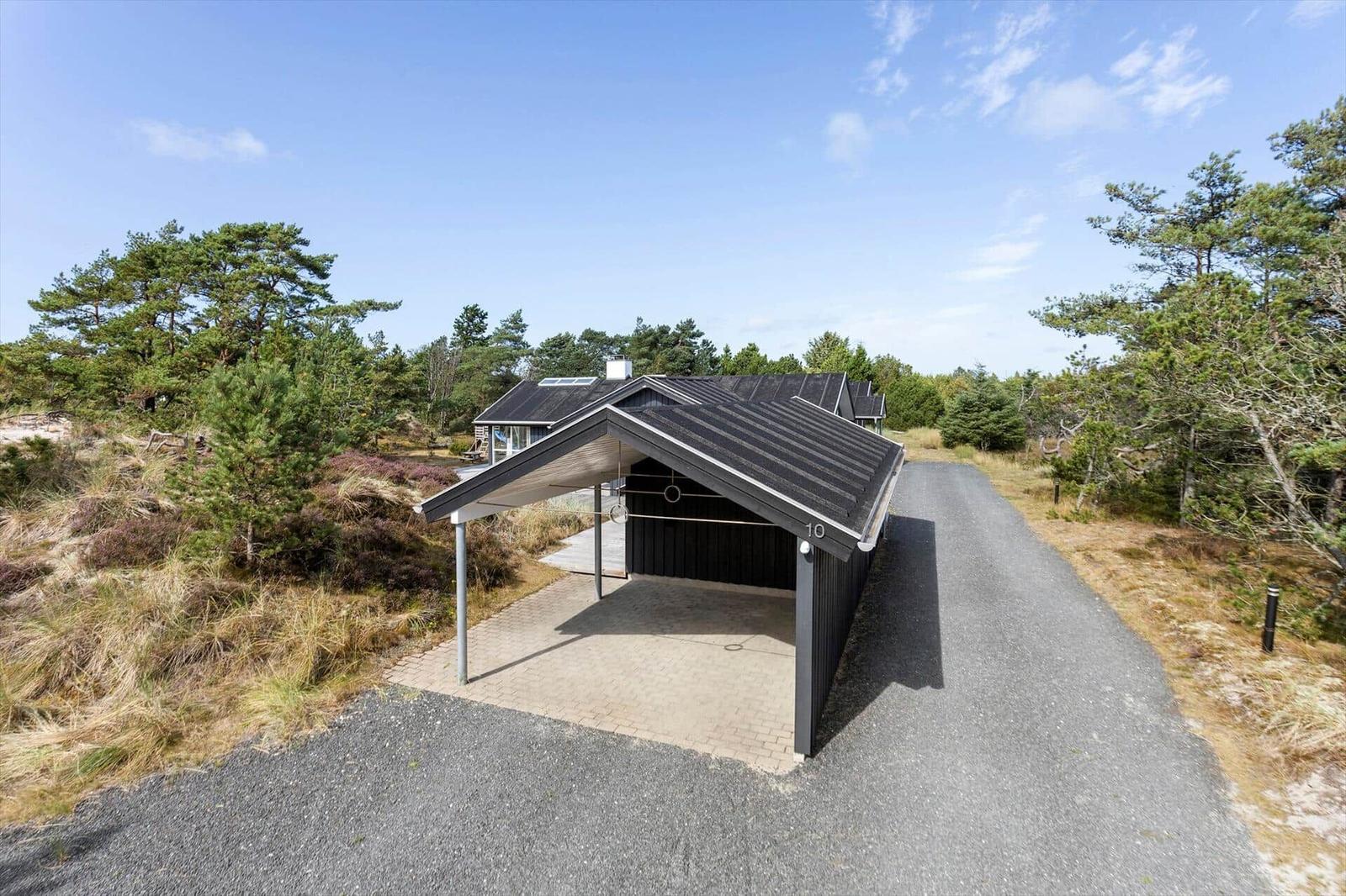 Schwarzer Holzcarport mit Steinfußboden vor dem Haus in Heide und Kiefern.