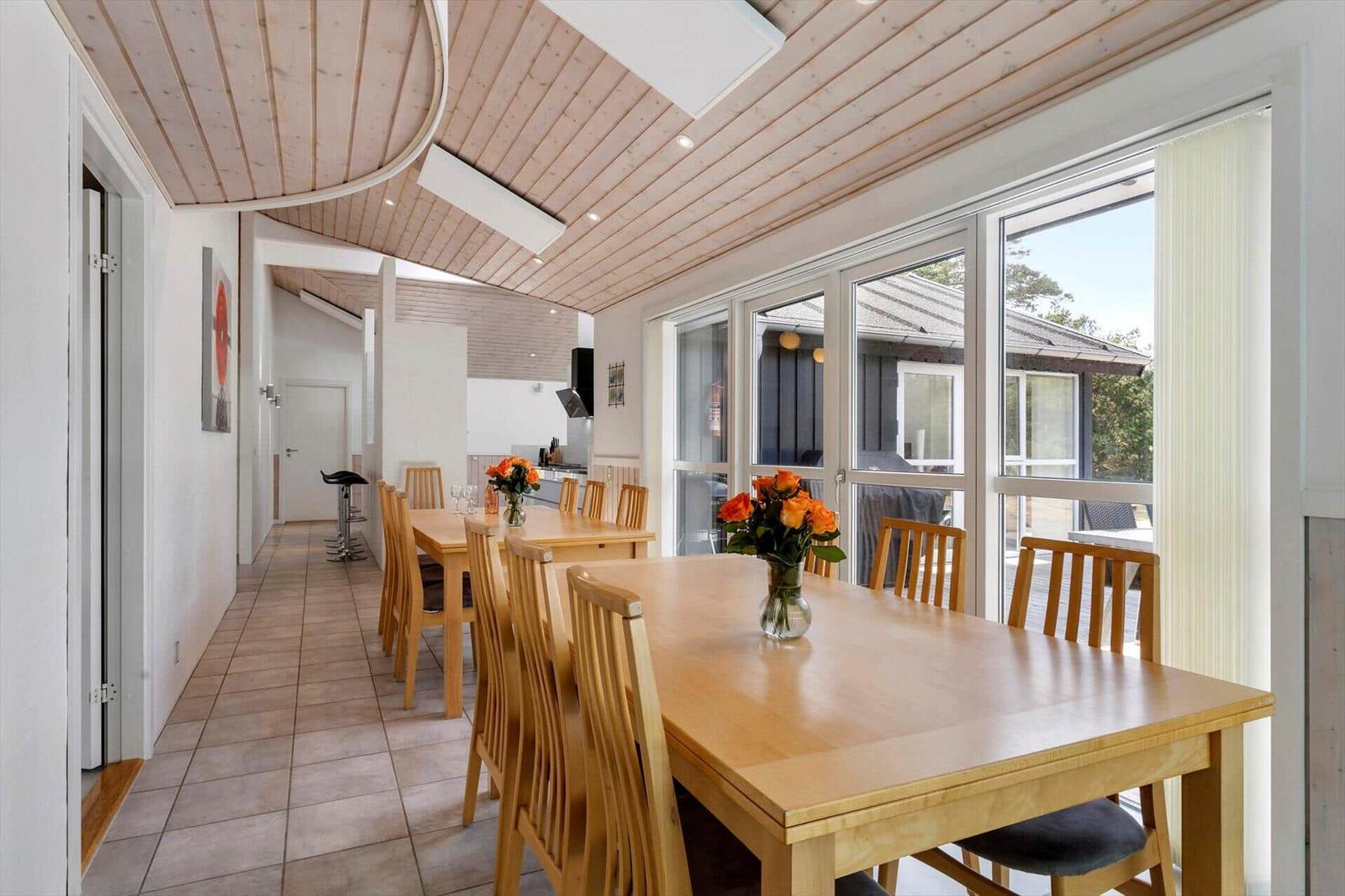 Essbereich mit zwei Holztischen, Stühlen, Rosen und Fensterfront zur Terrasse.