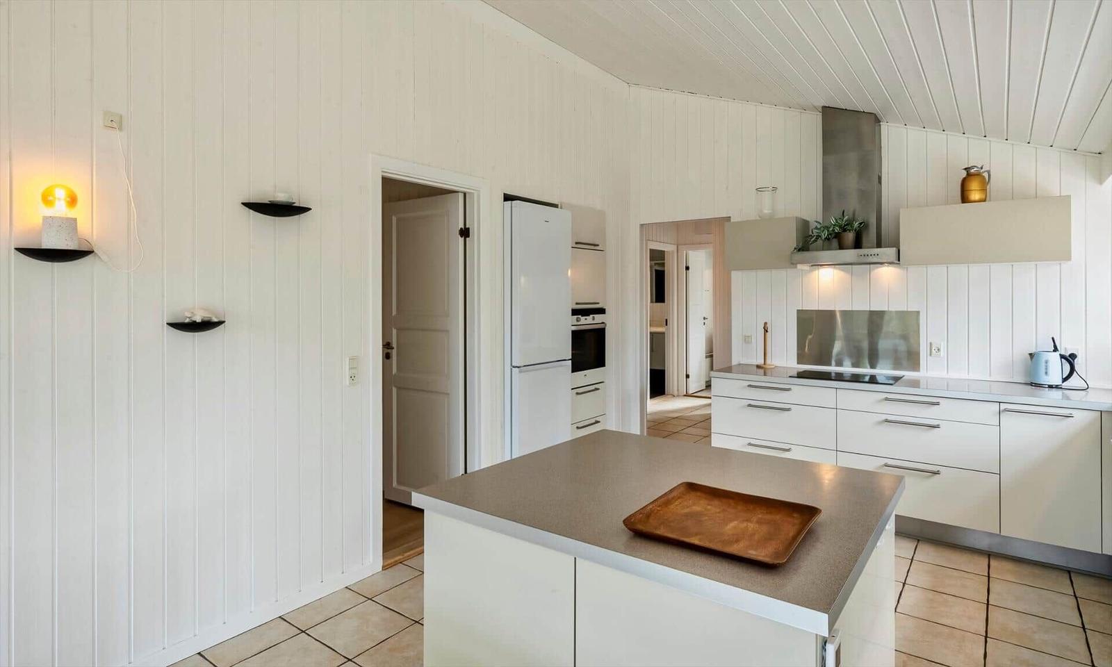 Küche mit weißer Insel, Ceranfeld, Dunstabzug, Backofen und Kühlschrank.