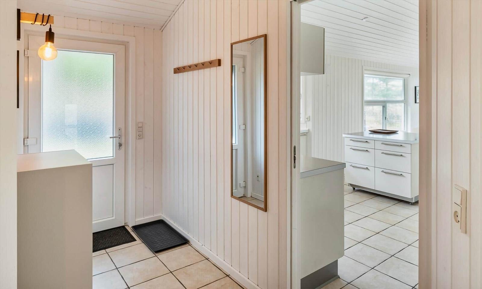 Flur mit Eingangstür, Garderobe, Spiegel und Durchgang zur hellen Küche.