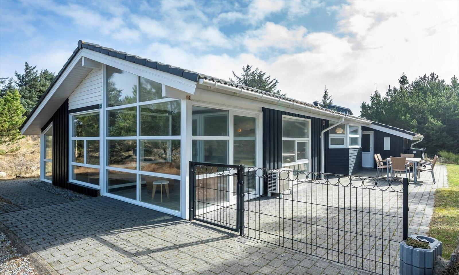 Schwarzes Holzhaus mit Glasfront, Steinterrasse, Metallzaun und Gartensitzgruppe.