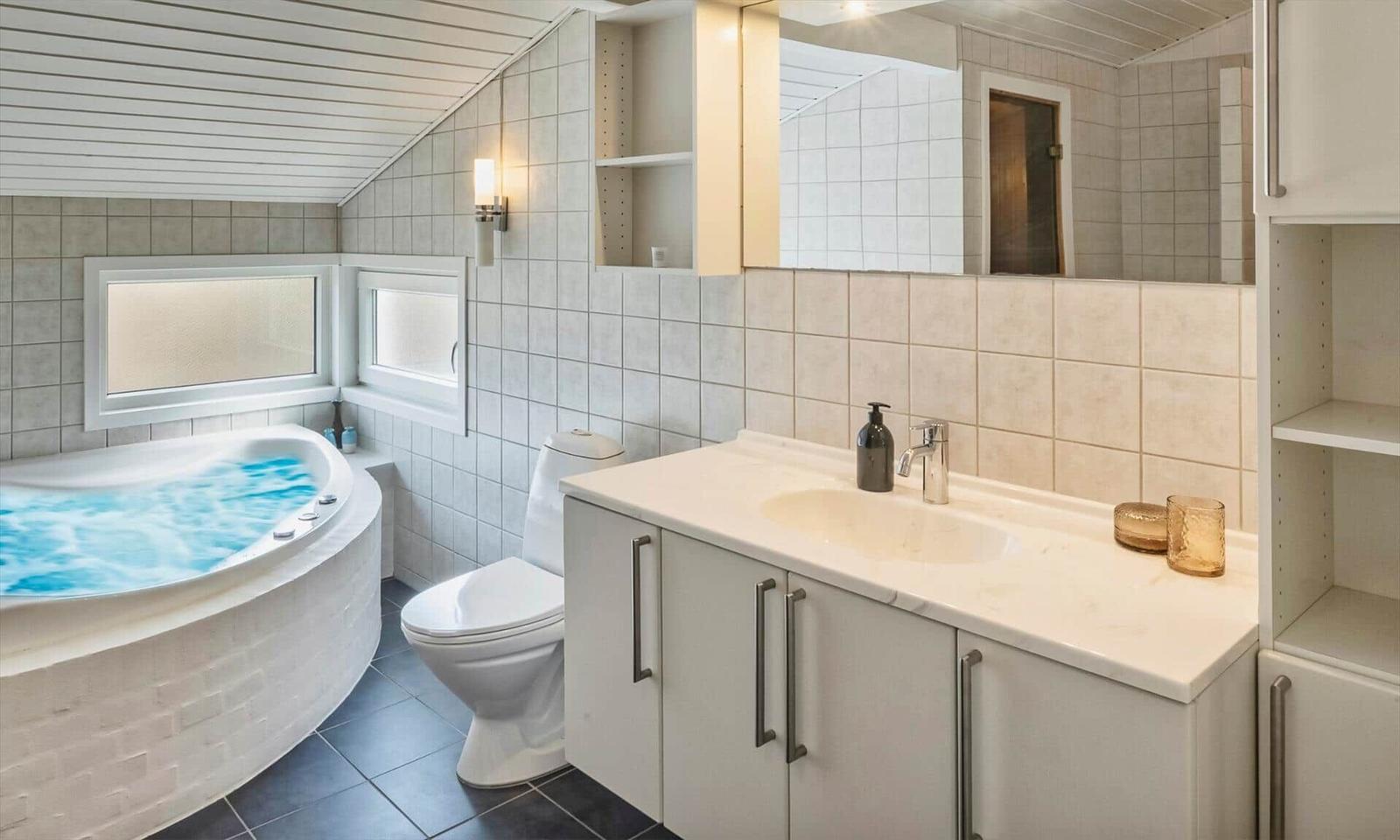 Badezimmer mit rundem Whirlpool, Toilette, Waschtisch und dunklen Fliesen.