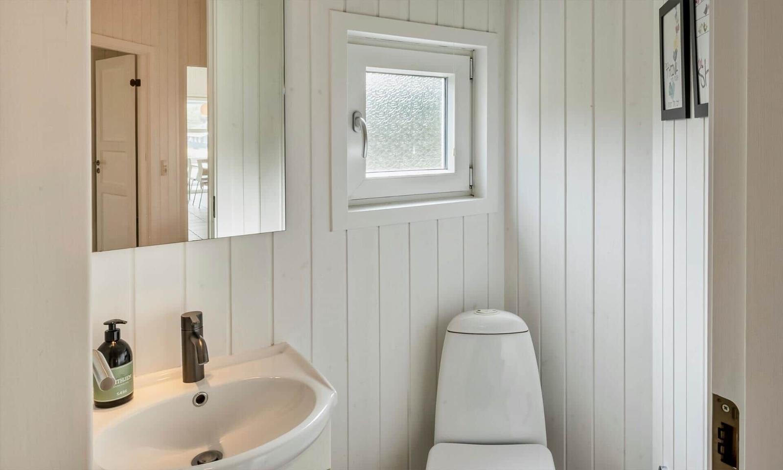 Gäste-WC mit Holzpaneelen, Waschbecken, Toilette und kleinem Fenster.