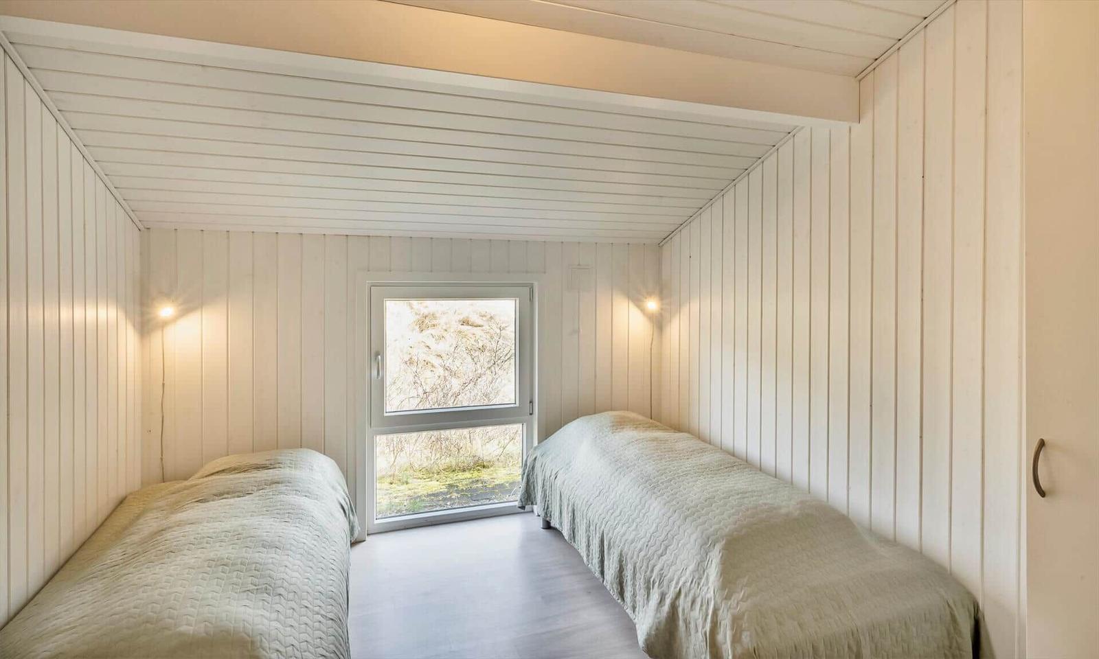 Schlafzimmer mit zwei Einzelbetten, Fenster und weißer Holzvertäfelung.