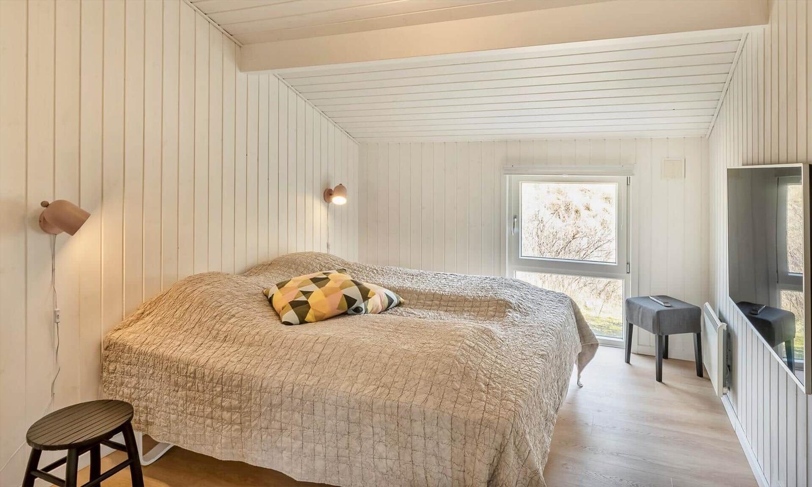 Schlafzimmer mit Doppelbett, Wandlampen, Fernseher und Dachschräge.