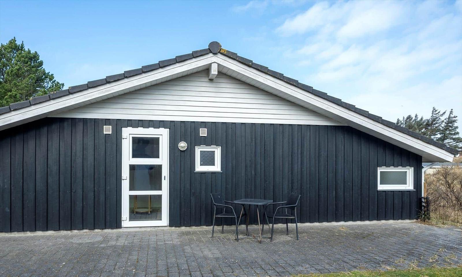 Schwarze Holzfassade mit weißem Giebel, Steinterrasse und kleiner Sitzgruppe.