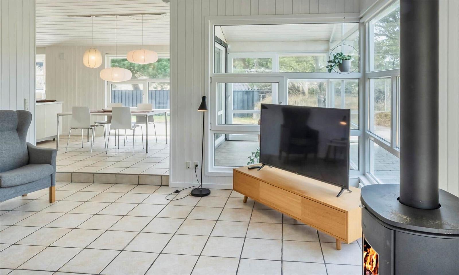 Wohnraum mit Kaminofen, Fernseher und erhöhtem Esstisch unter Pendelleuchten.