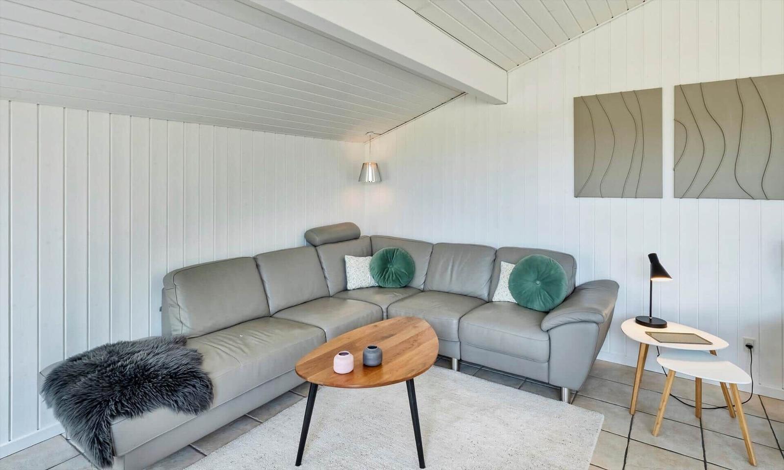 Graues Ecksofa mit grünen Kissen, Holzcouchtisch und weißen Beistelltischen.