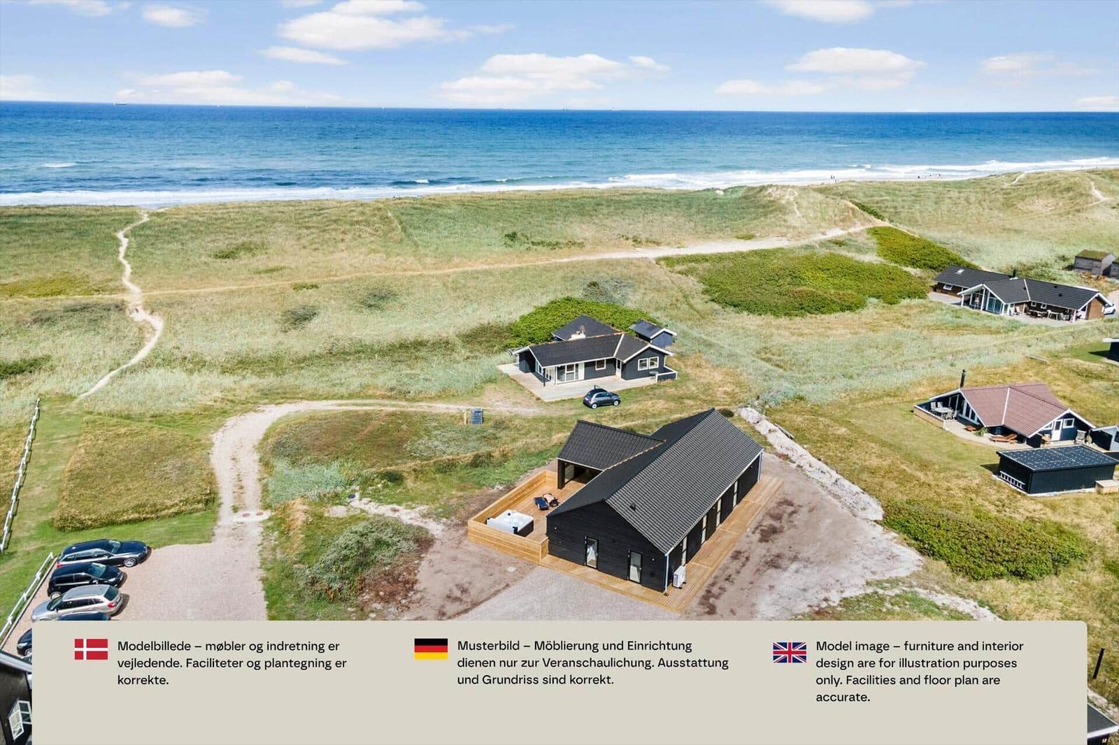 Luftbild eines schwarzen Holzhauses mit Terrasse und Whirlpool in den Dünen am Meer.