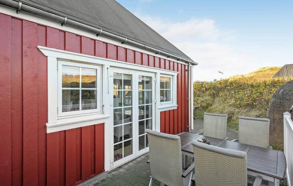 Terrasse am roten Holzhaus mit grauem Esstisch, vier Stühlen und Steinpflaster.