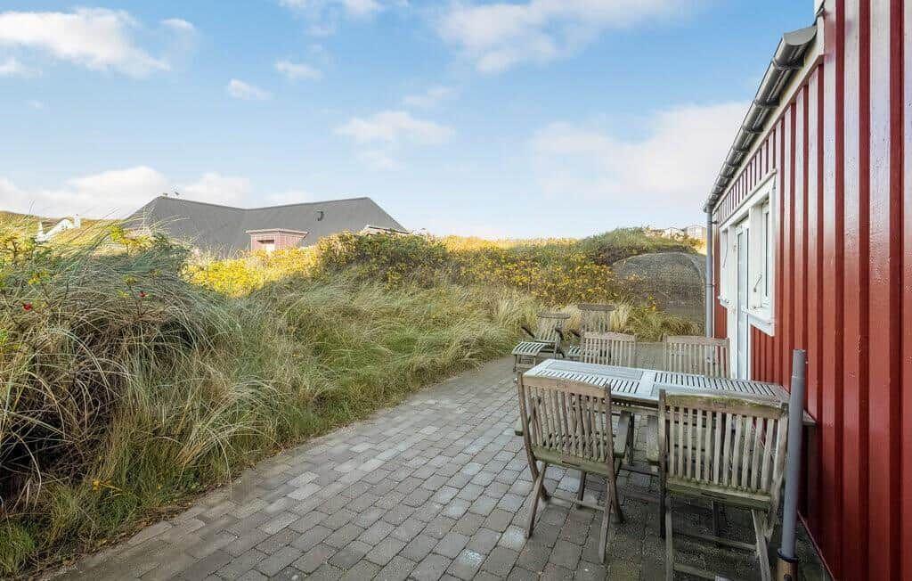 Gepflasterte Terrasse am roten Holzhaus mit Holzmöbeln und zwei Liegestühlen.