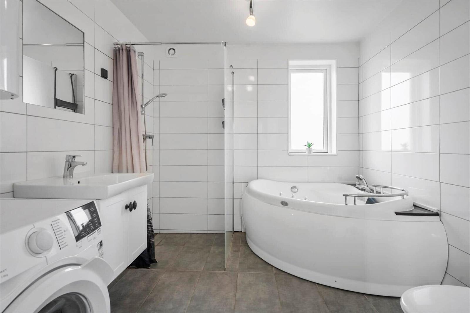 Bathroom with corner bathtub, glass shower, vanity and washing machine.