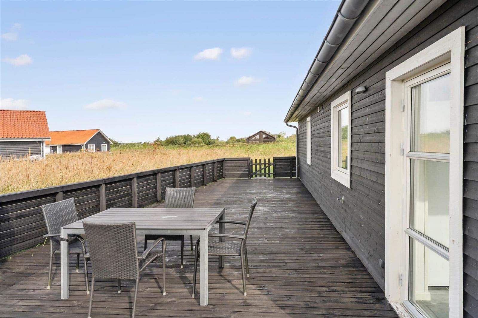 Wooden terrace with grey dining table and four chairs next to a glass door on the dark house.