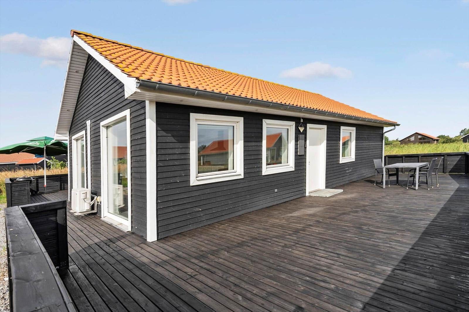 Black wooden house with white windows, dining set on the terrace and tiled roof.