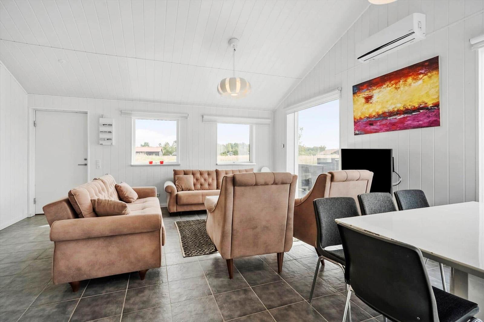 Bright living area with beige sofas, dining table, TV and colorful wall painting.
