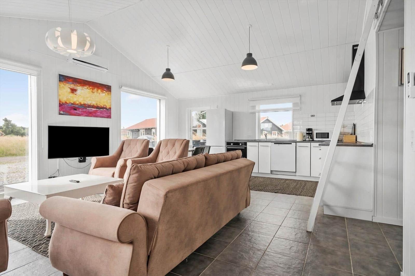 Open plan living area with beige sofa, white kitchen units, TV and loft ladder.