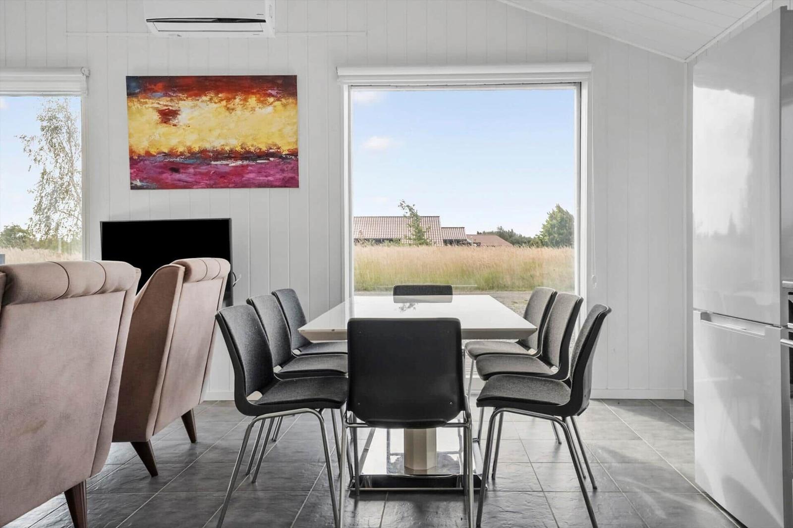 Dining area with white table, black chairs, large window and colorful wall painting.