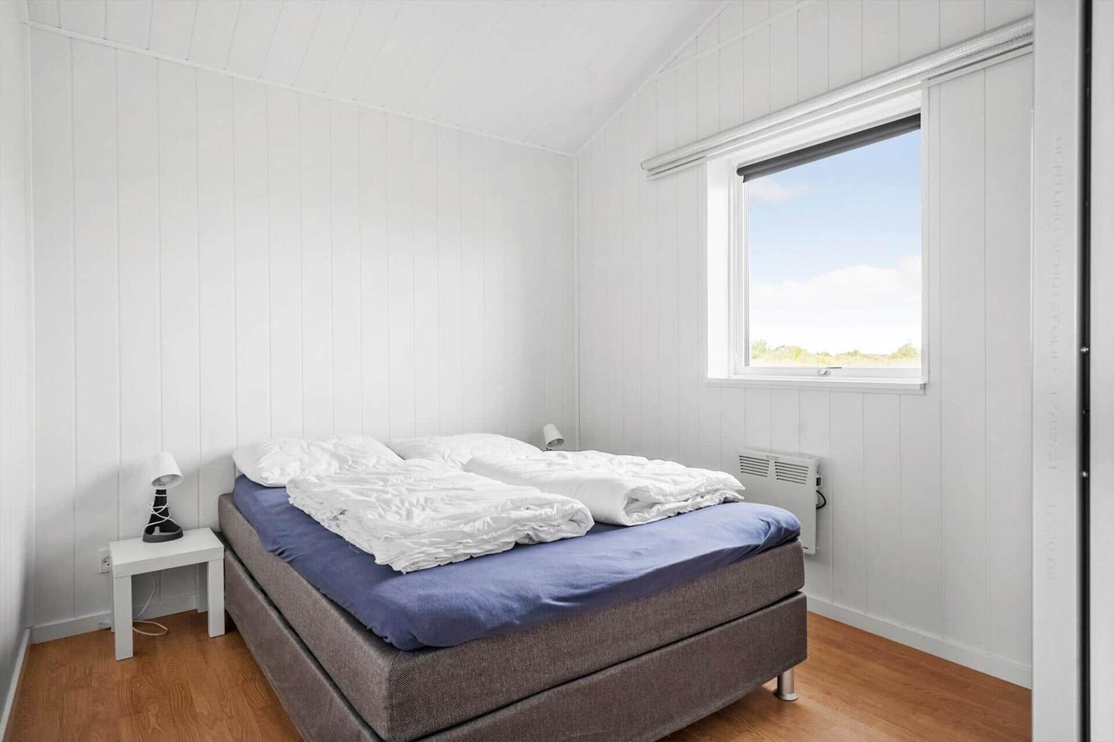 Bedroom with double bed, two white duvets, window and a bedside lamp.