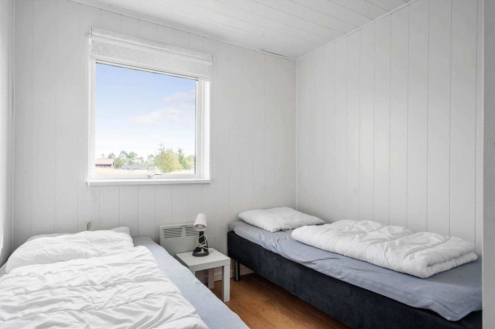 Bedroom with two single beds at a right angle, window and white nightstand.