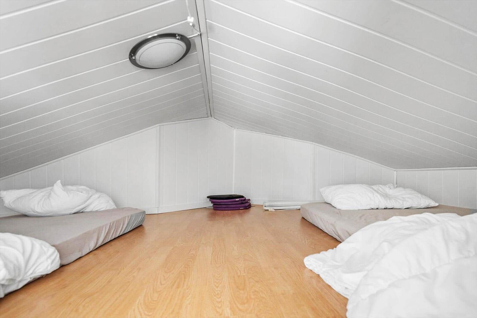 Sleeping loft with two mattresses on the floor under a white paneled sloped ceiling.
