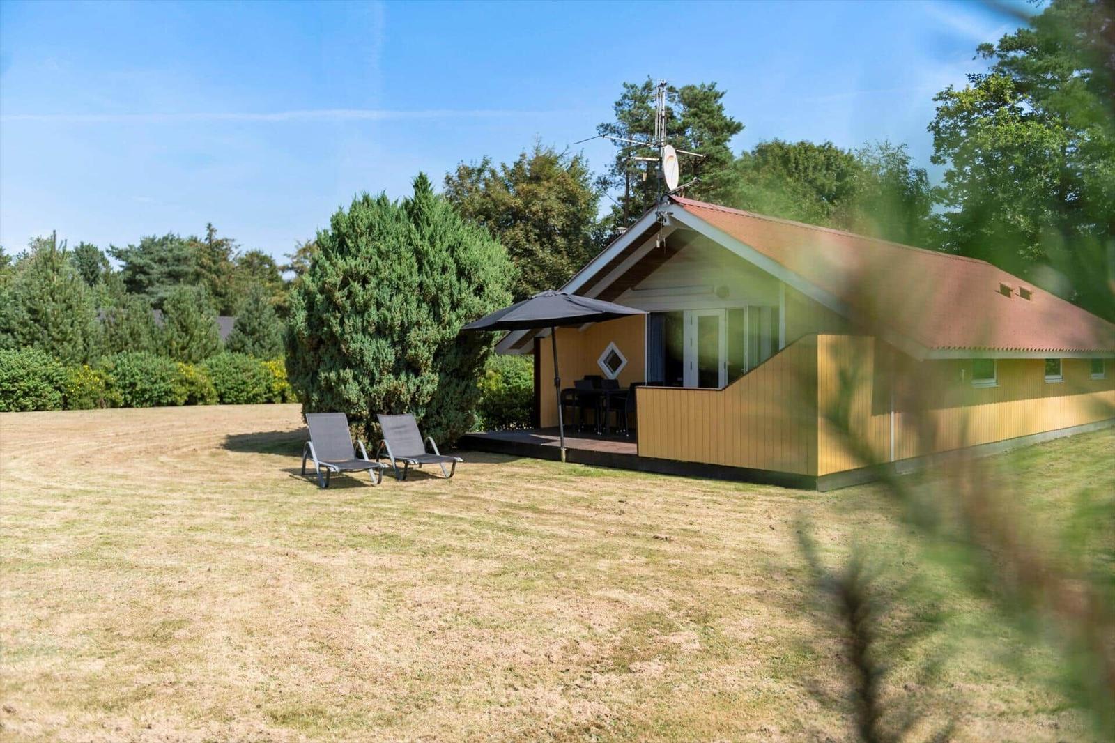 Yellow wooden house with terrace, parasol, garden furniture and two loungers.
