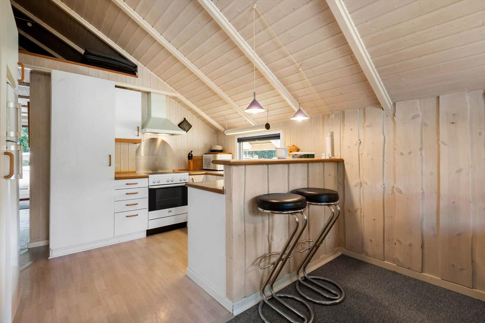 Open kitchen with white cabinets, wooden breakfast bar and two bar stools.