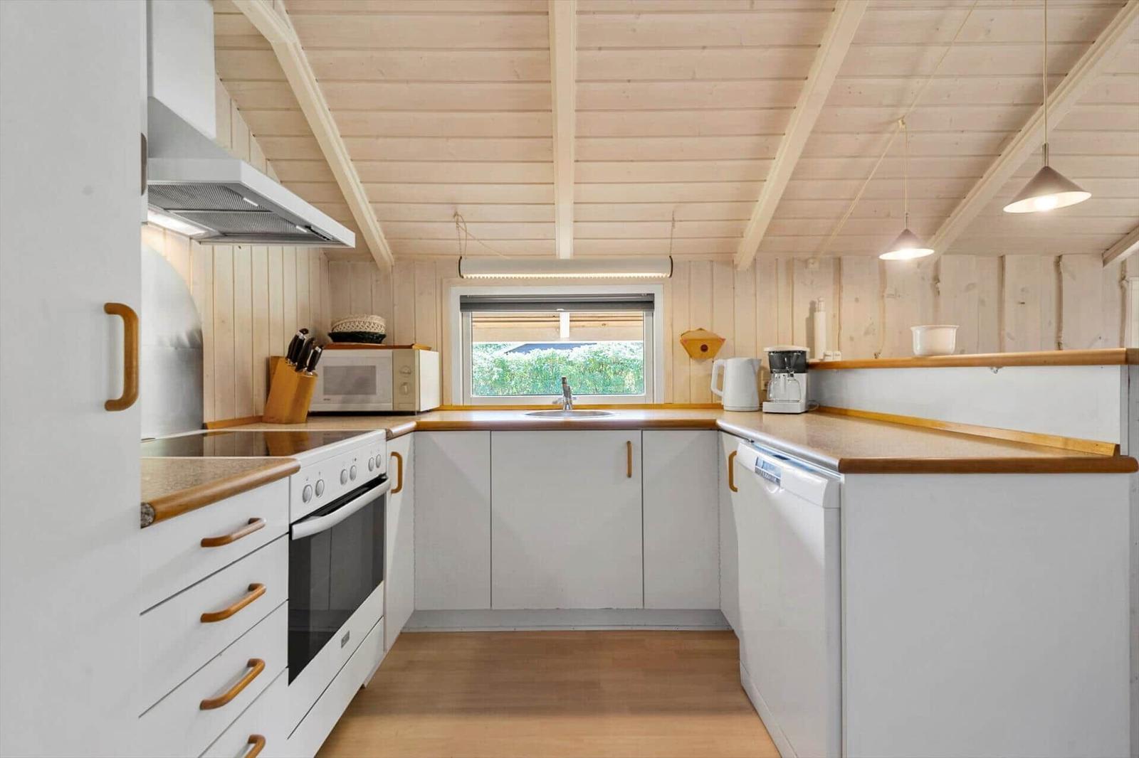 White U-shaped kitchen with wood worktop, stove, sink, dishwasher and microwave.