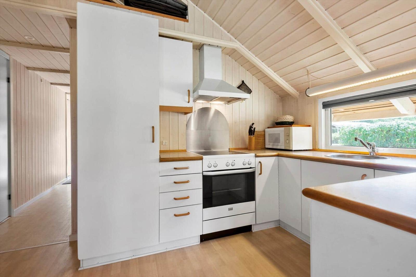 Kitchen with white tall cabinet, stove, microwave and sink at the window.