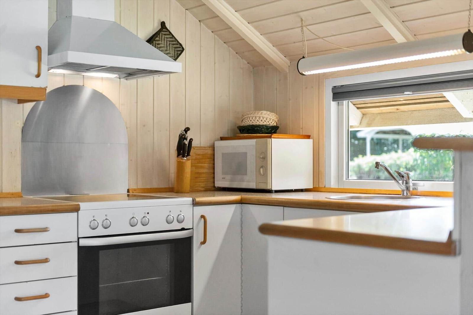 Kitchen wall with white stove, extractor hood, microwave and sink under sloped ceiling.