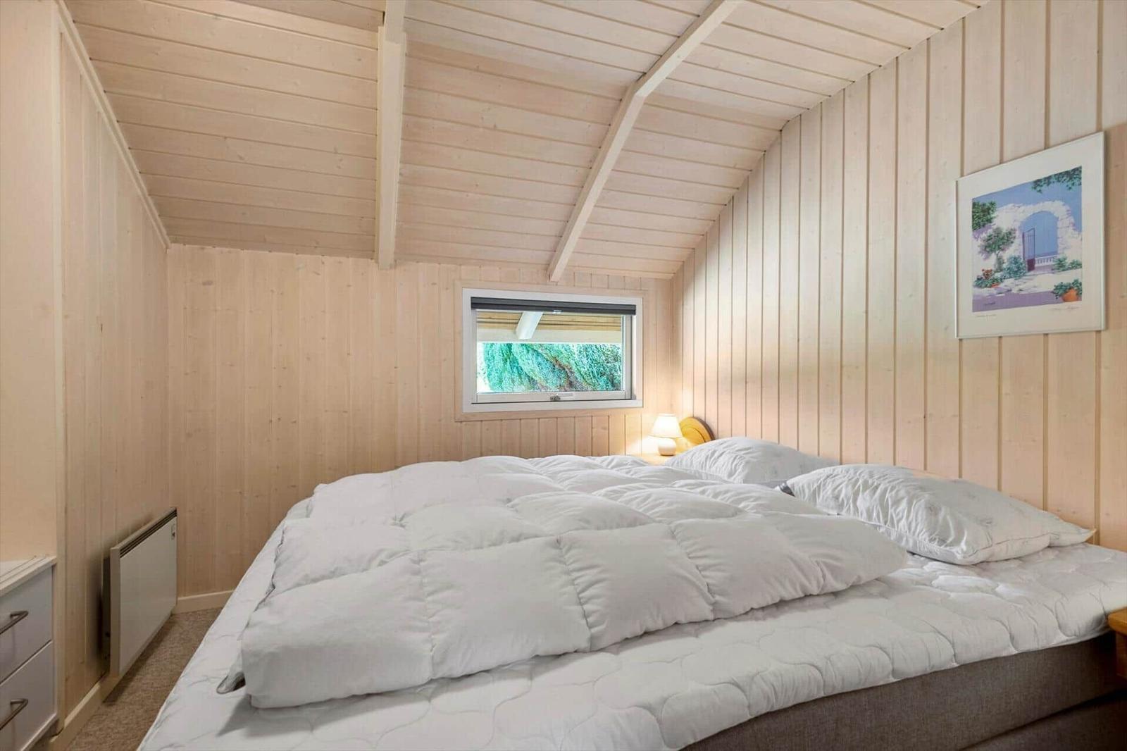 Bedroom with wood panels, double bed with white duvet and a small window.