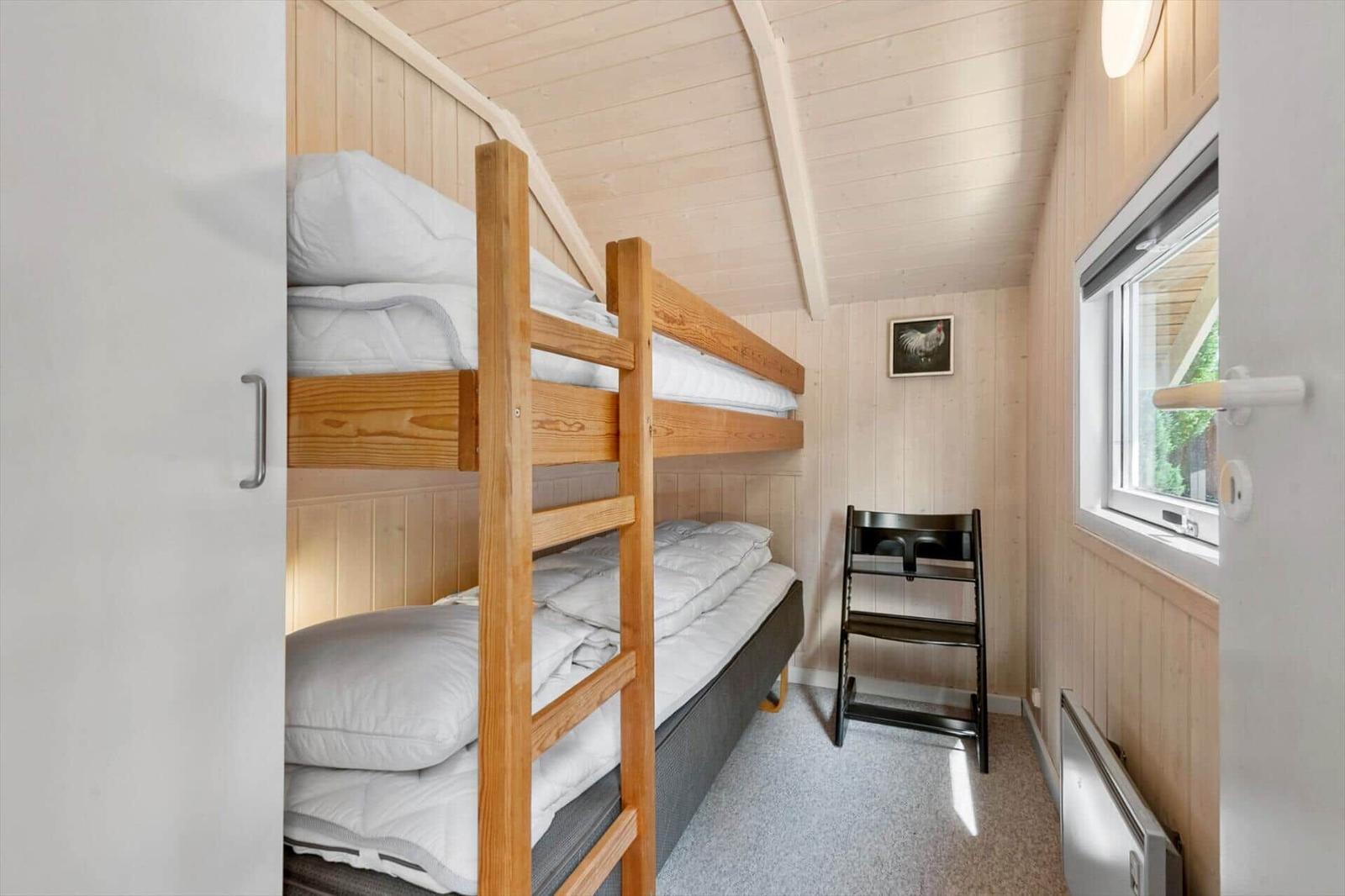 Bedroom with wooden bunk bed, white bedding and a small window.