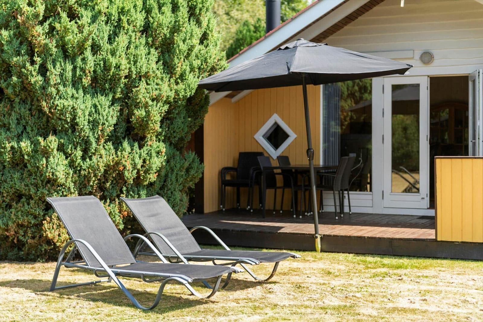 Lawn with two loungers in front of a wooden deck, dining table and open parasol.