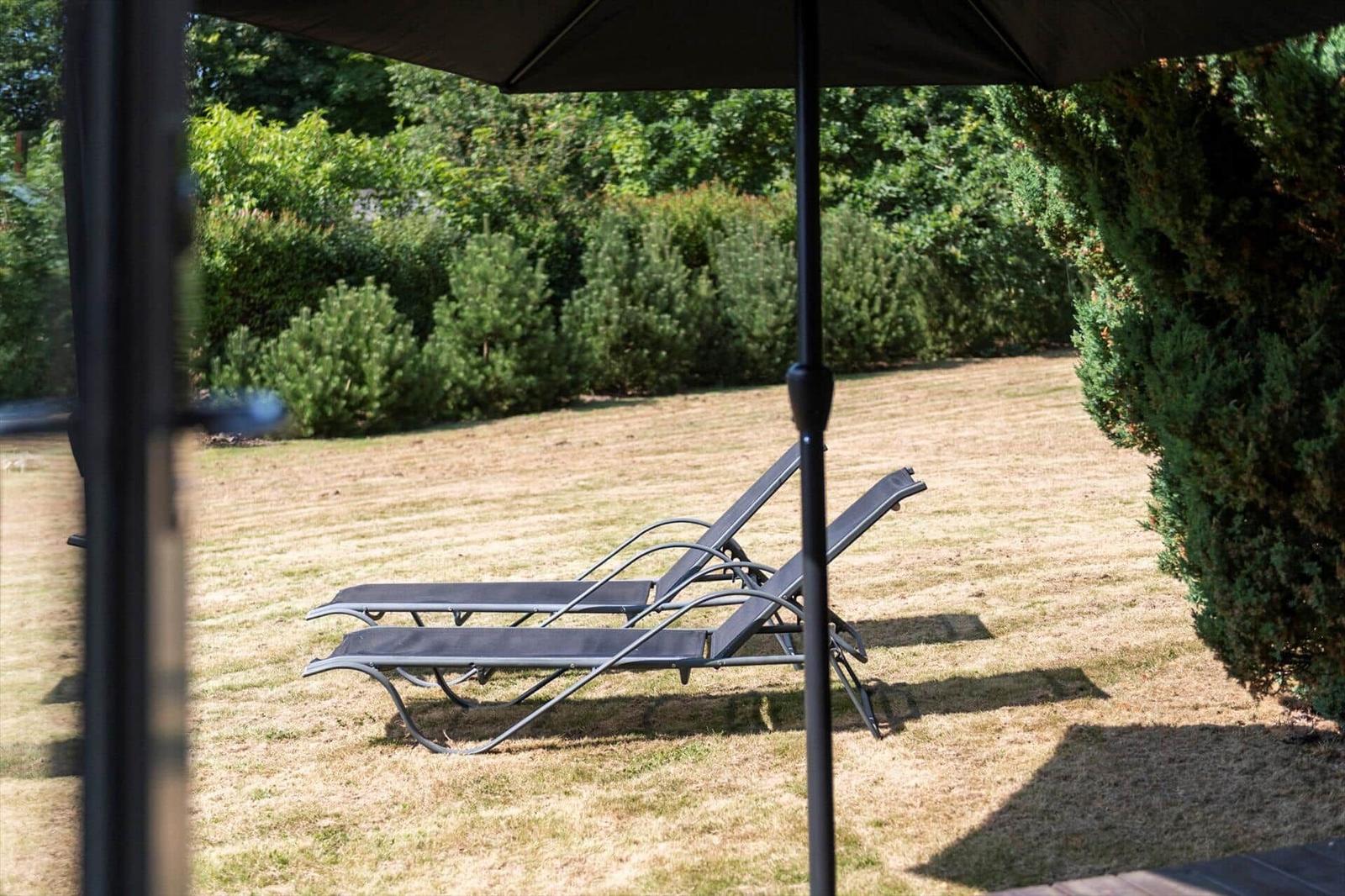 Two black sun loungers on a lawn under a parasol in front of a hedge.