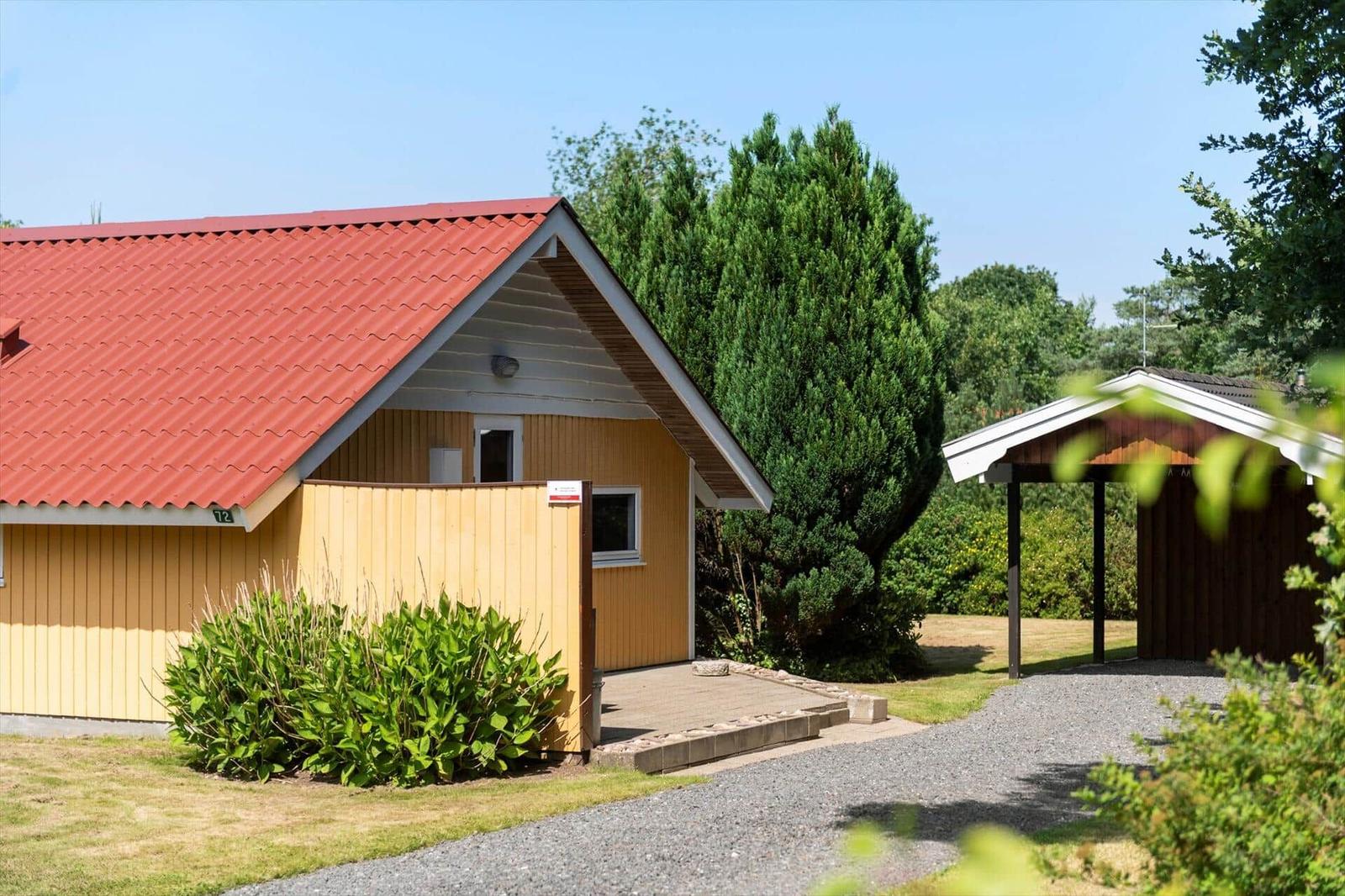 Yellow wooden house with red roof, privacy fence, carport and gravel path.
