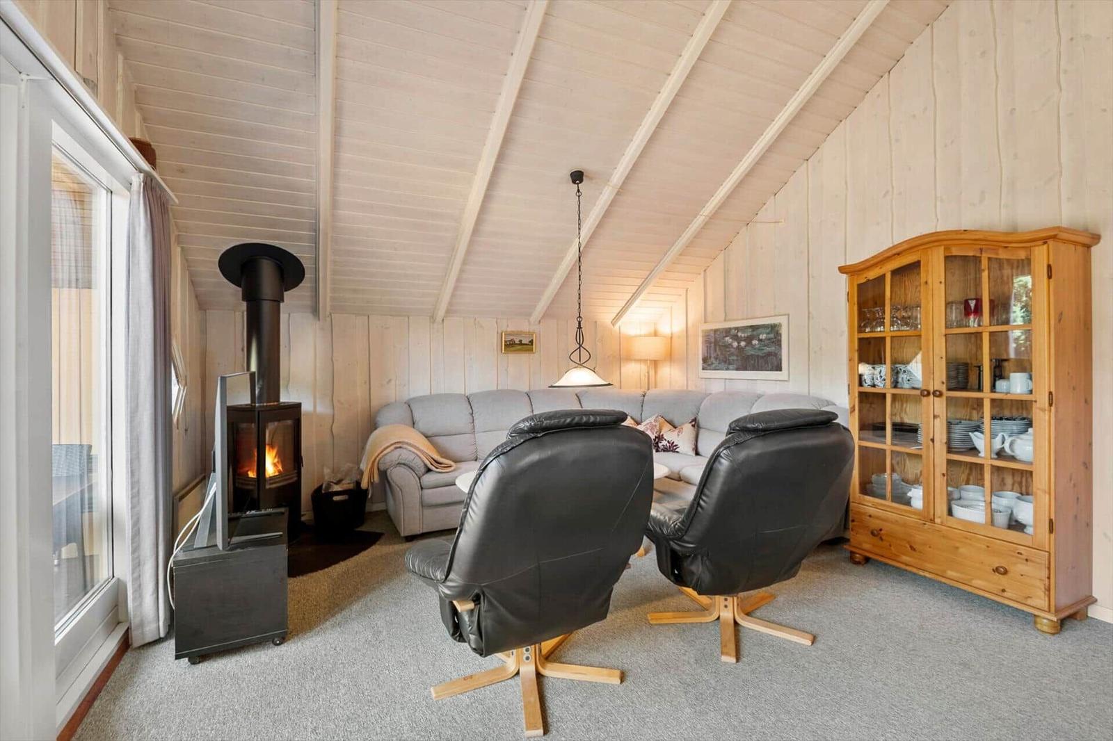 Living area with wood stove, grey sofa, leather armchairs and wooden cabinet.
