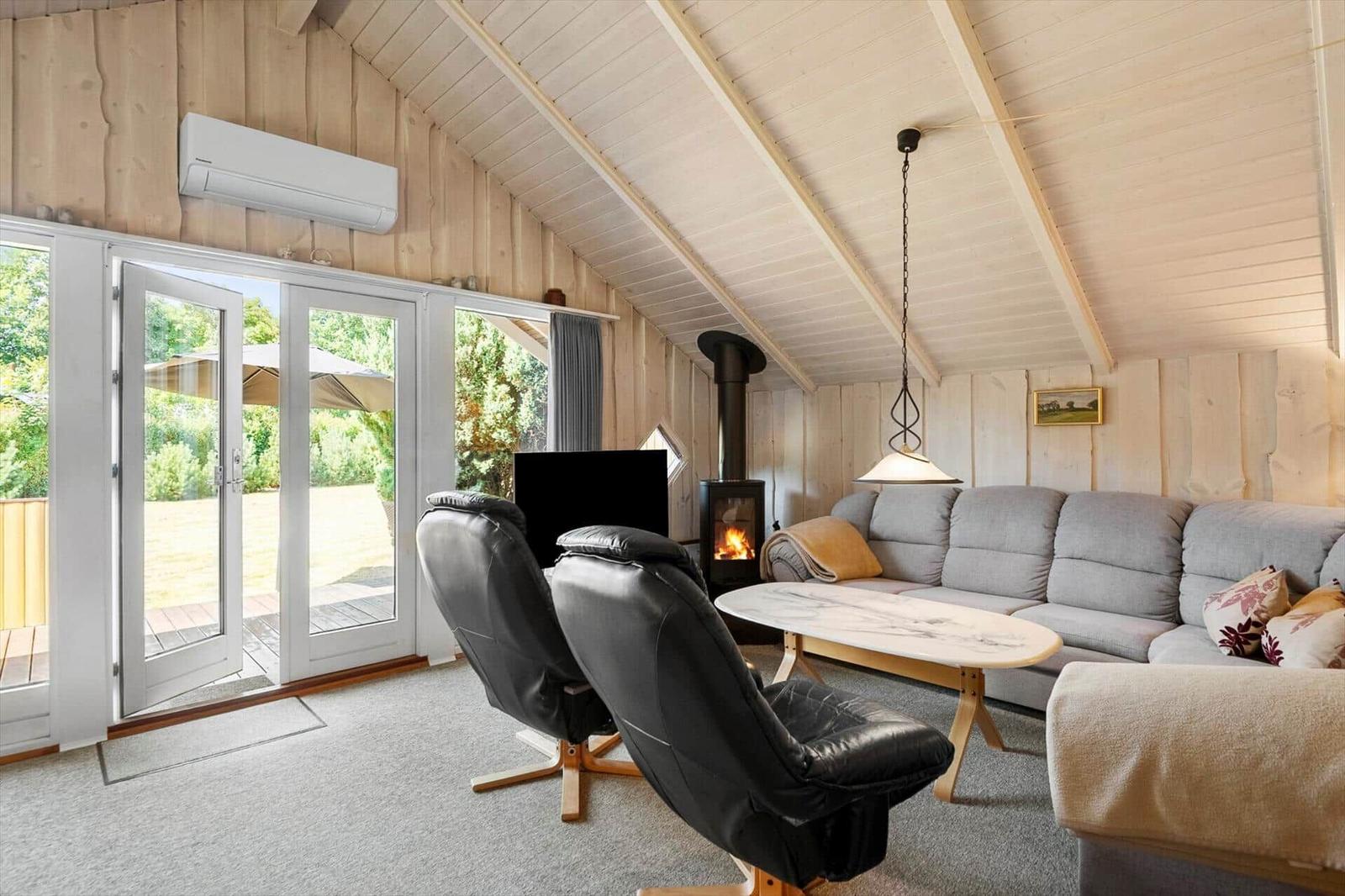 Living room with wood stove, corner sofa, leather chairs and open terrace doors.