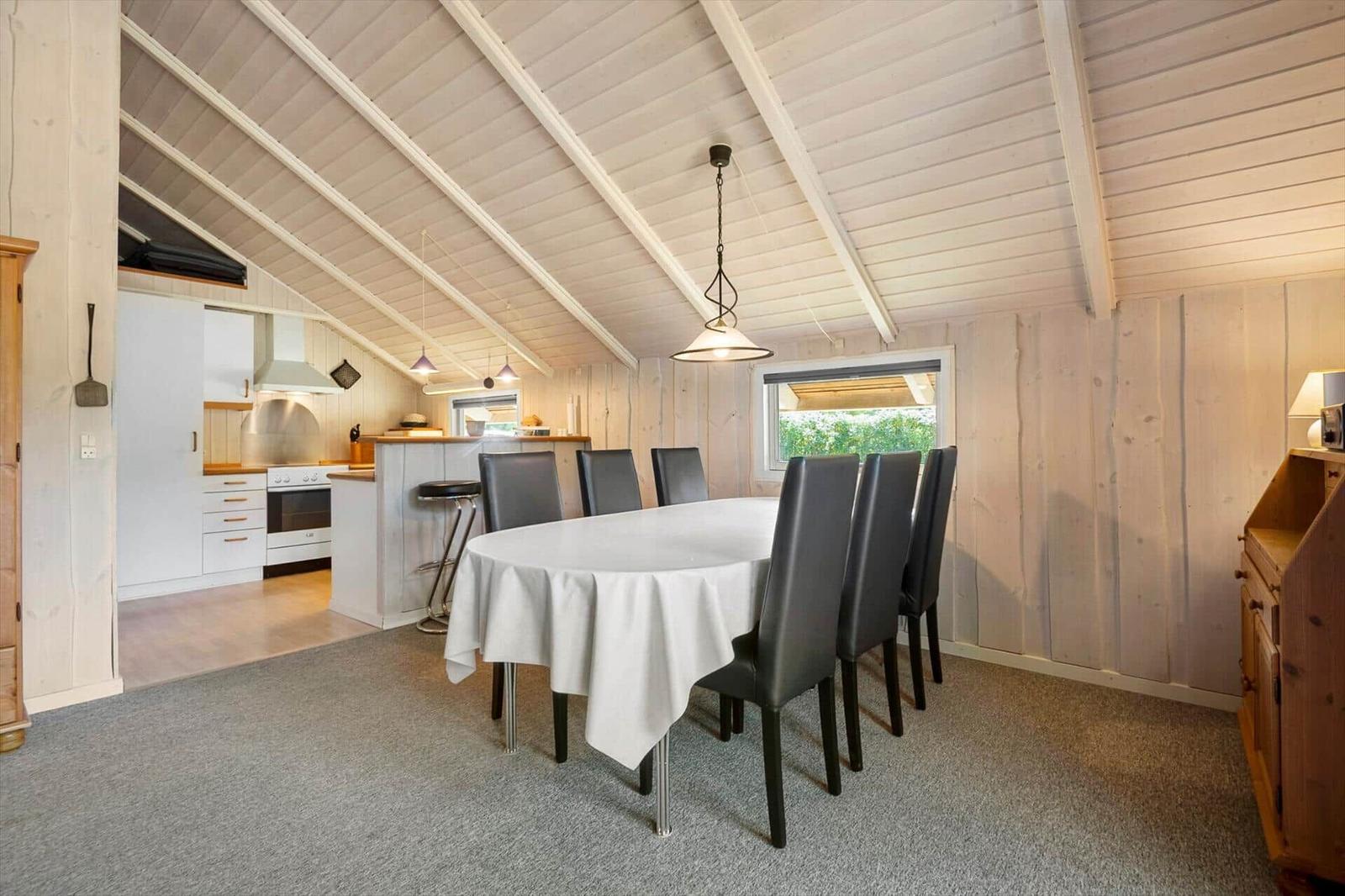 Dining area with white tablecloth, black chairs and an open kitchen.