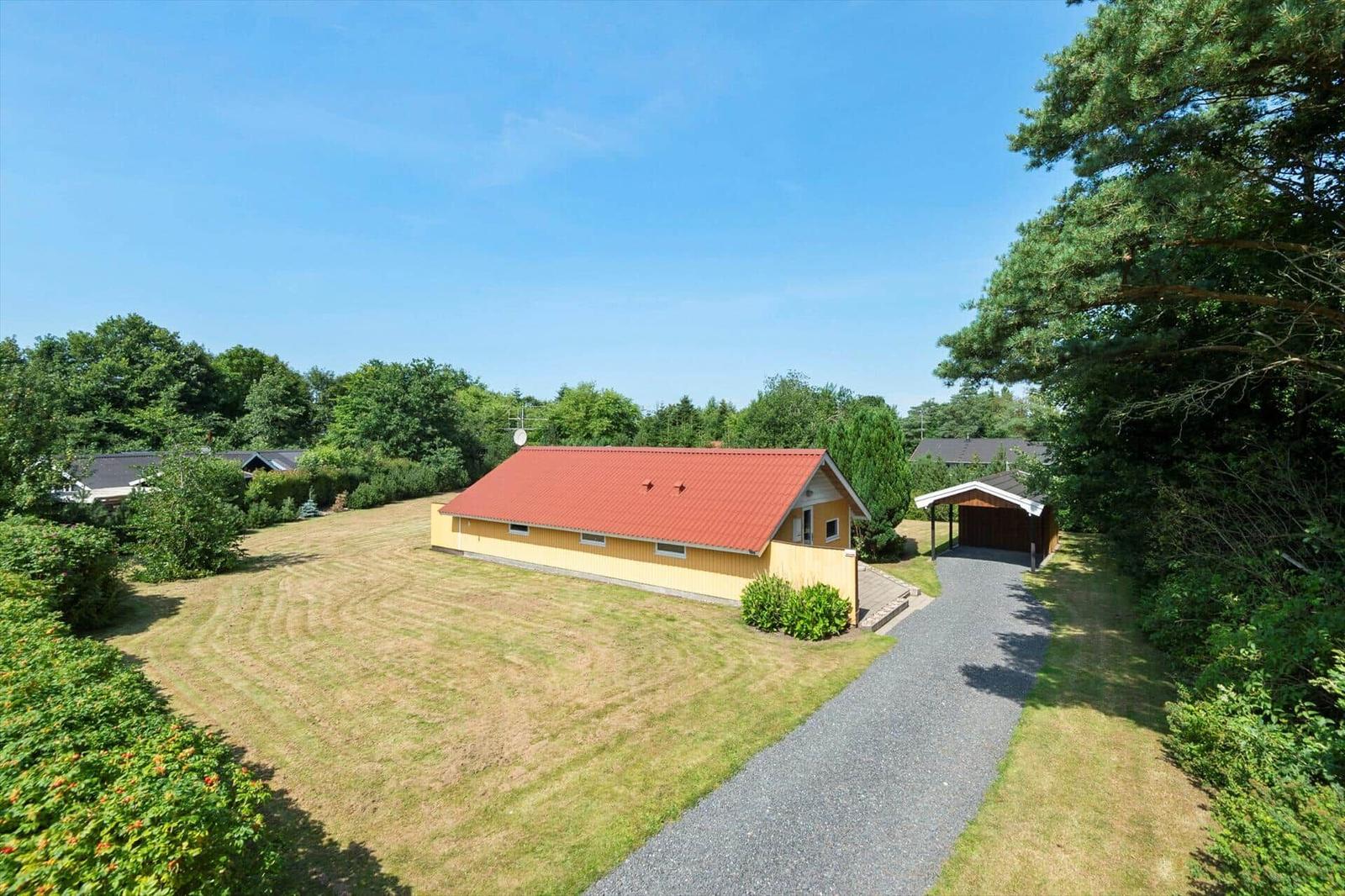 Yellow wooden house with red tiled roof, lawn, gravel drive and carport.