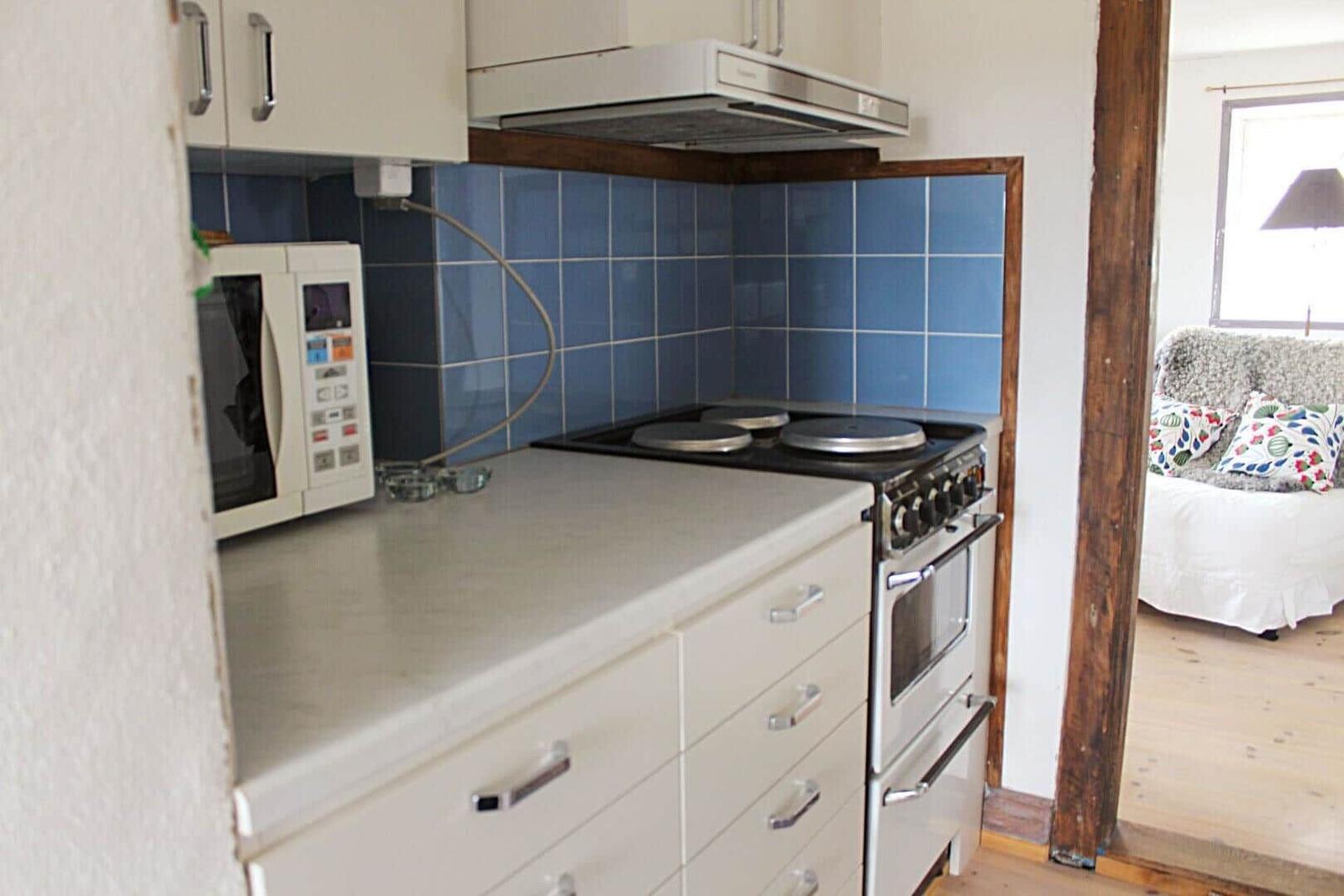 Ein Wohnzimmer mit grauem Sofa, weißem Sessel und runden Tisch. Drei Fenster und Teppich.