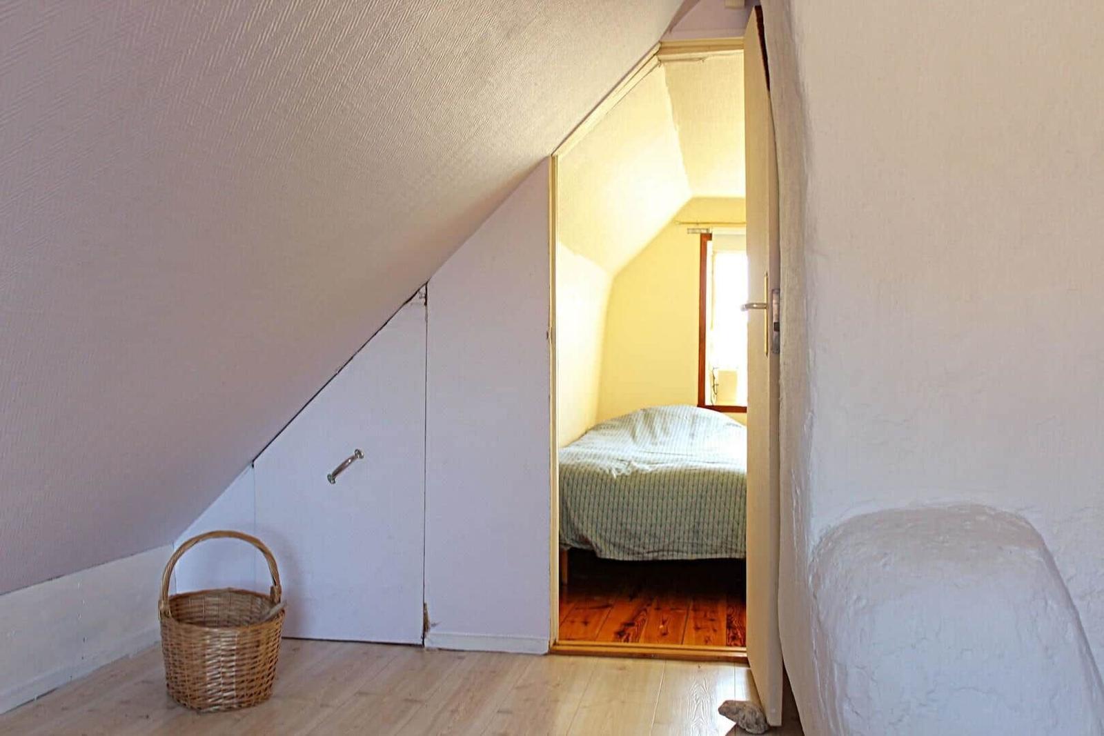 Schlafzimmer mit Dachschrägen, Bett mit gemustertem Bettzeug, Nachttisch und Fenster.