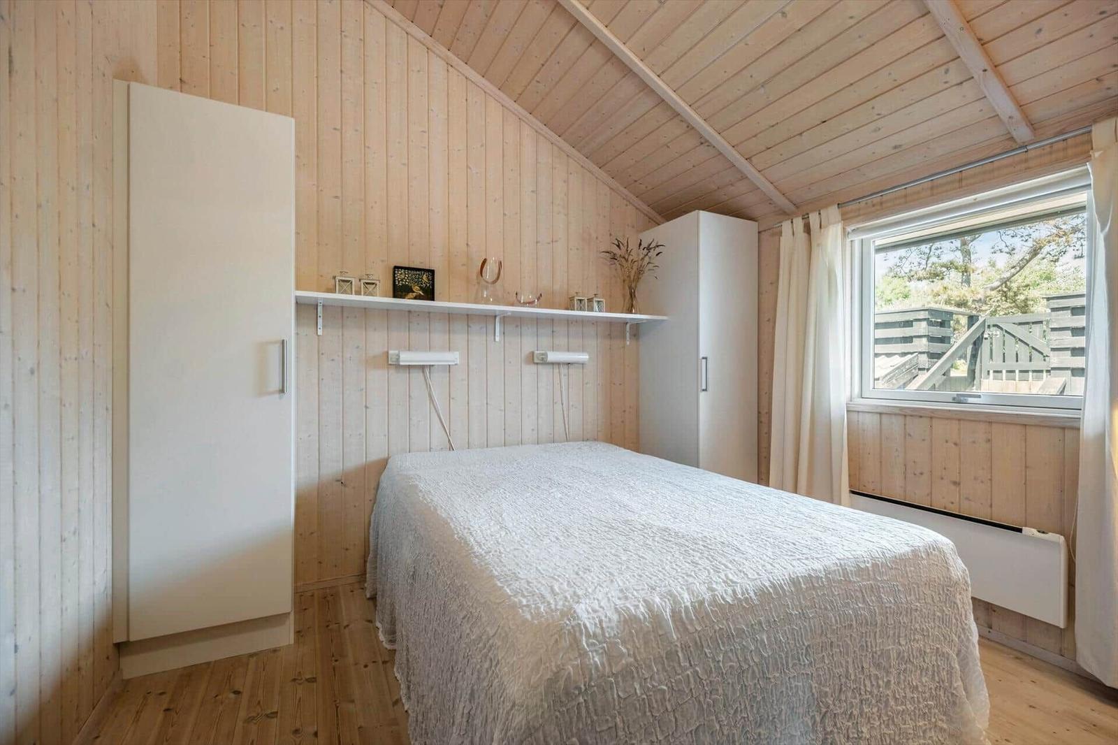 Schlafzimmer mit Holzwand, Bett, Nachttischen und Fenster.