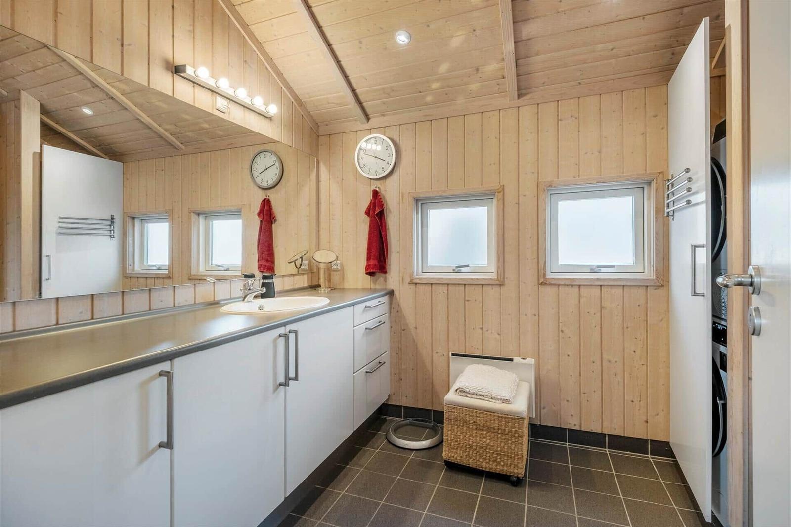 Badezimmer mit Holzwand, Waschbecken und Spiegel. Ein Fenster und ein Handtuch sind sichtbar.