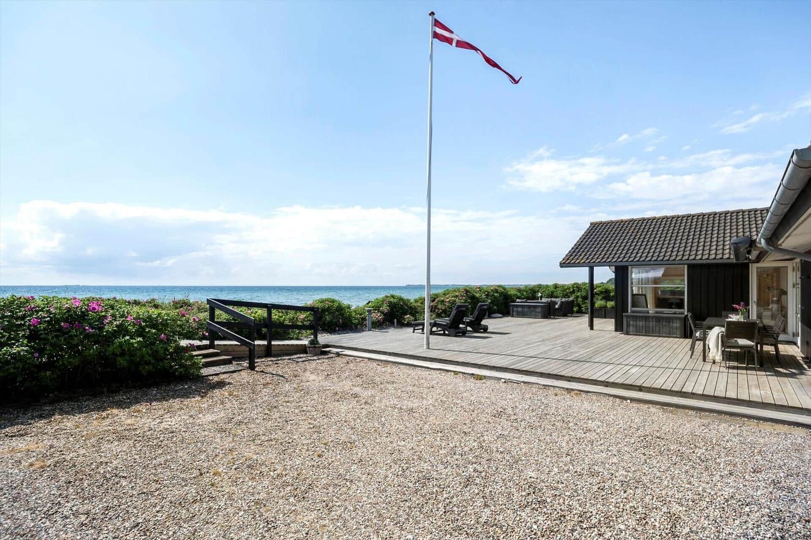 Holzterrasse mit Liegestühlen und Blick auf das Meer und grüne Pflanzen.