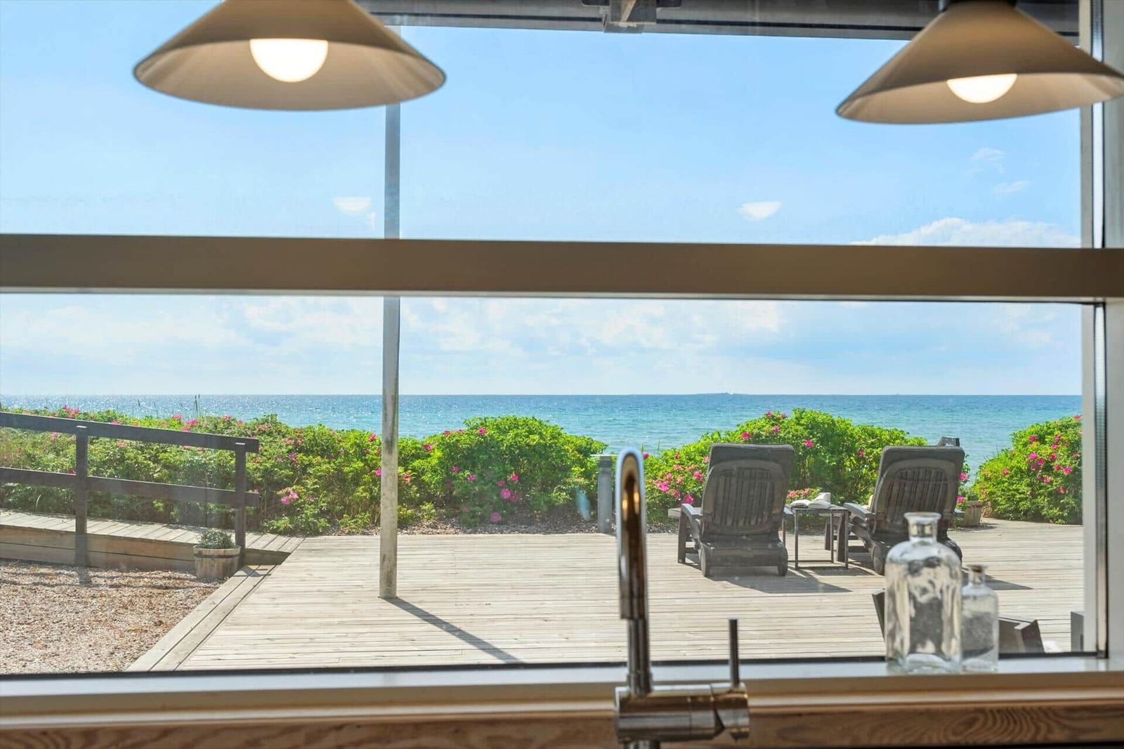 Küche mit Blick aufs Meer und Essbereich mit Holztisch und Stühlen.