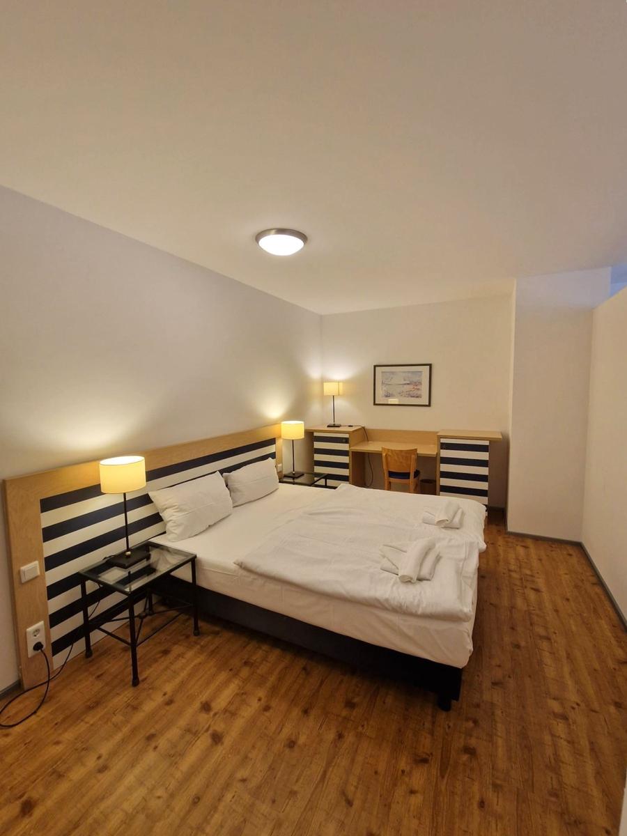Doppelbett mit weißer Bettwäsche, gestreiftem Kopfteil und Handtüchern.