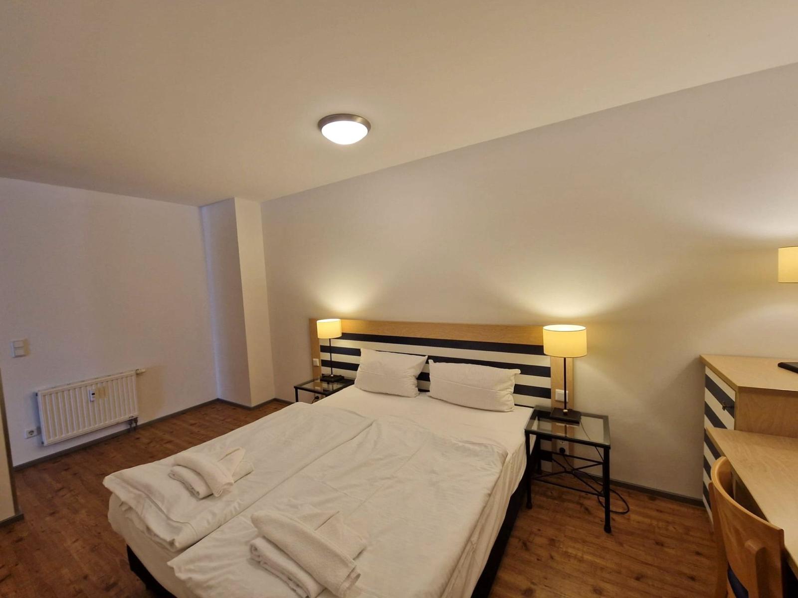 Doppelbett mit gestreiftem Kopfteil, zwei Nachttischlampen und Schreibtisch.