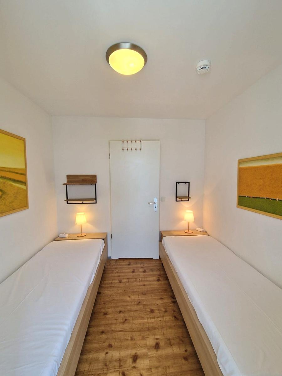Schlafzimmer mit zwei Einzelbetten, Nachttischlampen und Landschaftsbildern.