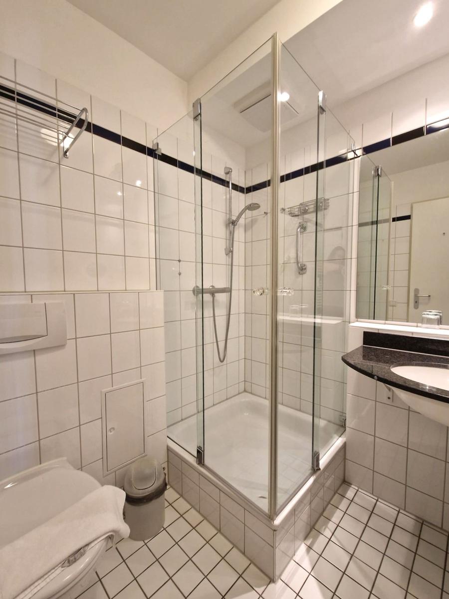 Bad mit Glasdusche, Hänge-WC und Waschbecken in dunkler Platte.