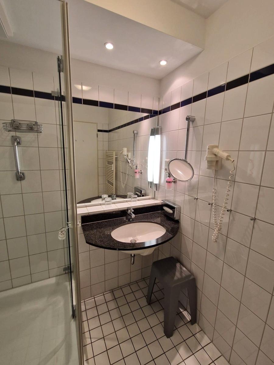 Bad mit dunklem Waschtisch, Spiegel, Föhn und Duschkabine.