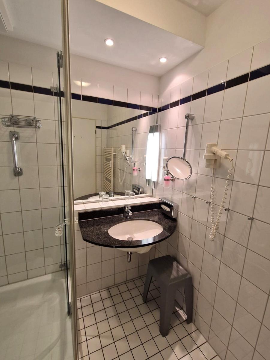 Bad mit dunklem Waschtisch, Kosmetikspiegel, Föhn und grauem Hocker.